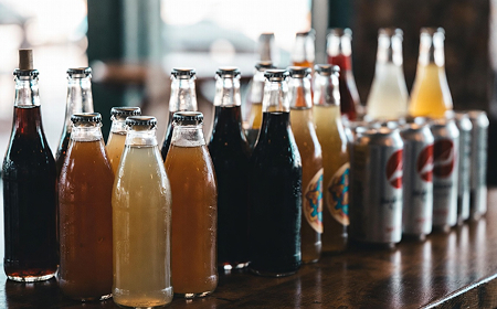 Ряд стеклянных бутылок и банок с разноцветными напитками на деревянном столе